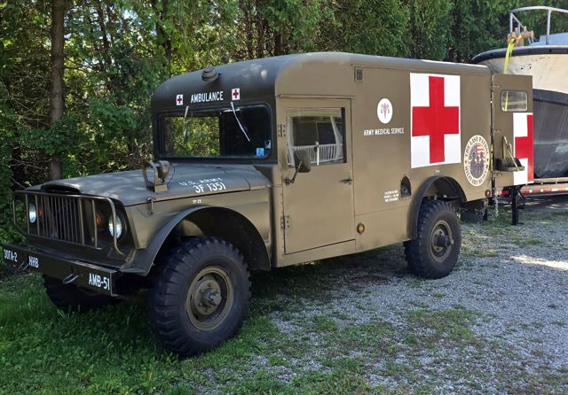 The Kaiser Jeep M725 ambulance outdoors, front three-quarter view, with the Army Medical Service cross and The Last Patrol roundel