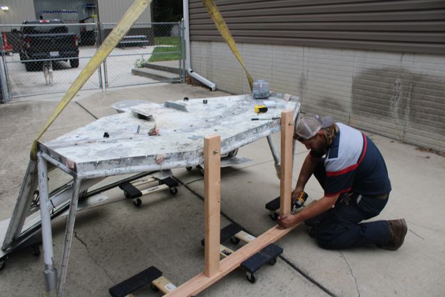 The removed pilothouse roof on a wooden cradle with a volunteer working on it