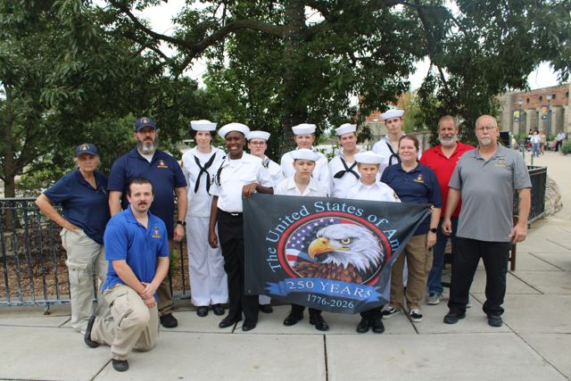 Sea Cadets and adult volunteers holding a United States of America 250 Years banner
