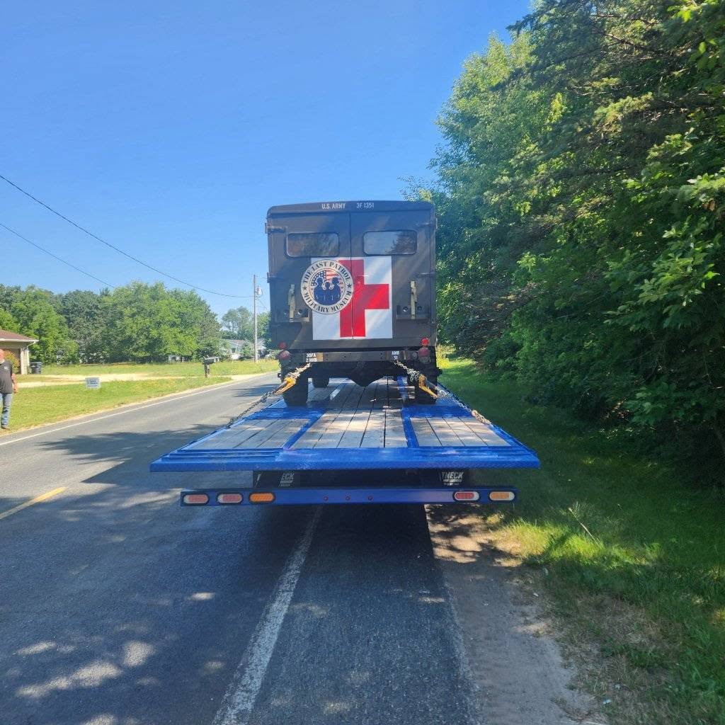The M725 military ambulance loaded for transport, wearing The Last Patrol Military Museum roundel beside its red cross